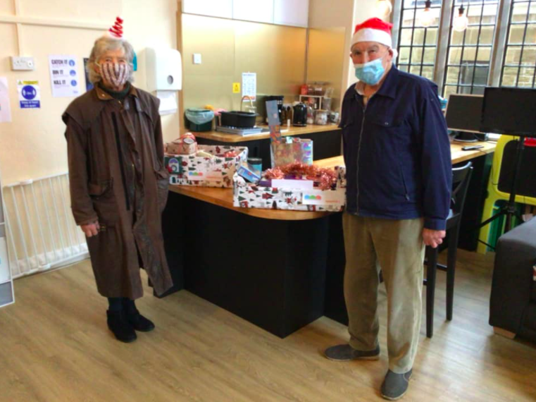 2 volunteers observing social distancing & masks while posing with Christmas hampers